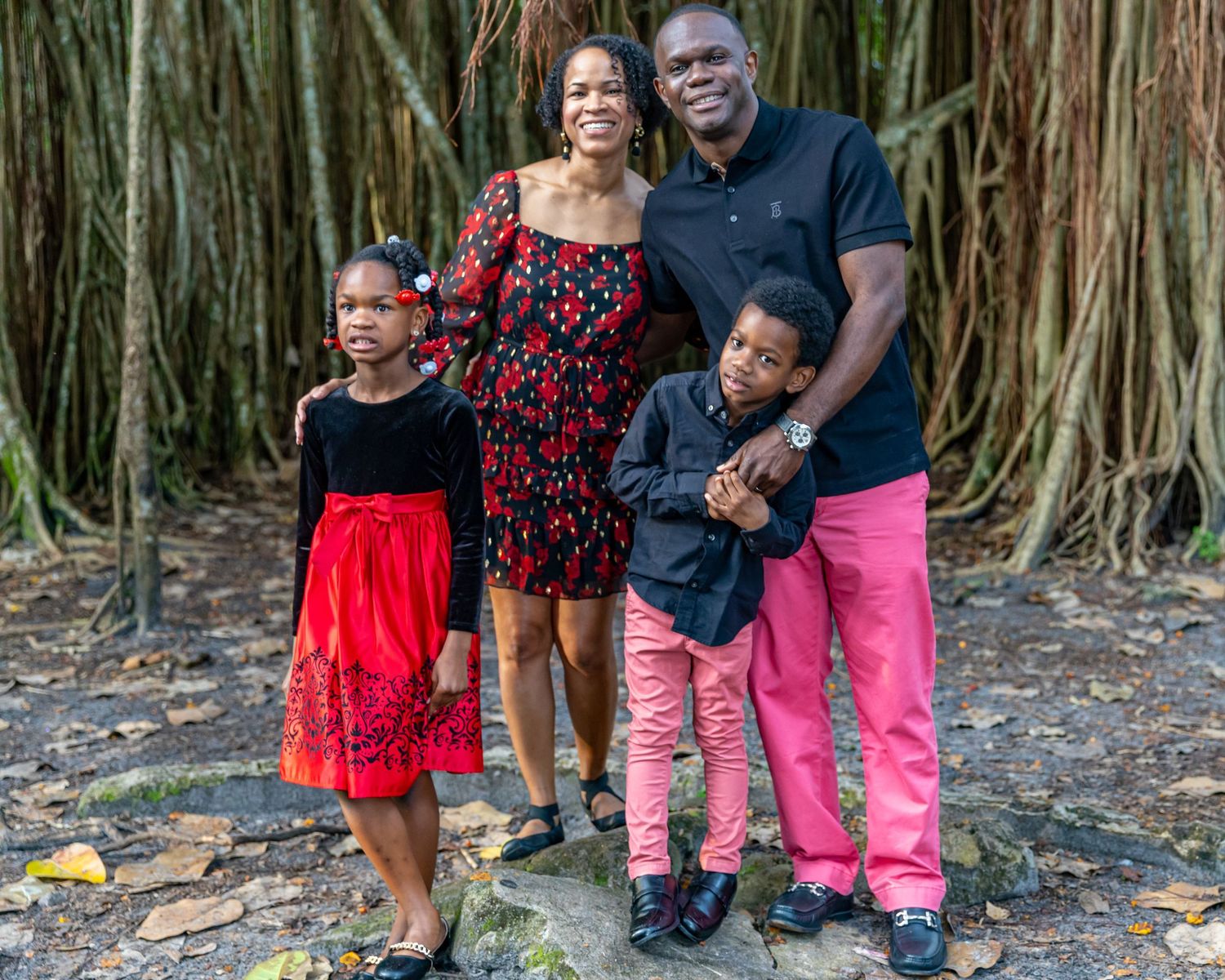 Family of four poses in coordinated outfits against a natural backdrop of tall banyan trees.