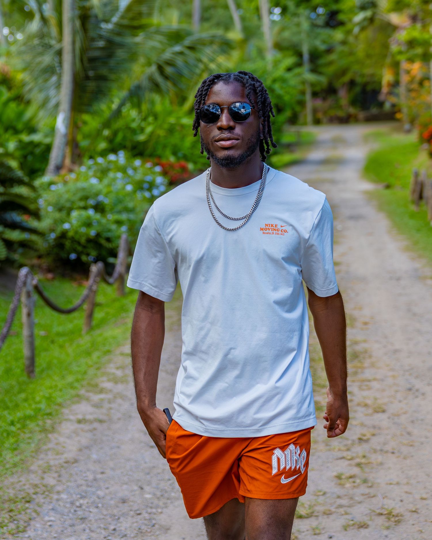 Casual styled person in Nike shirt and orange shorts poses on garden path.