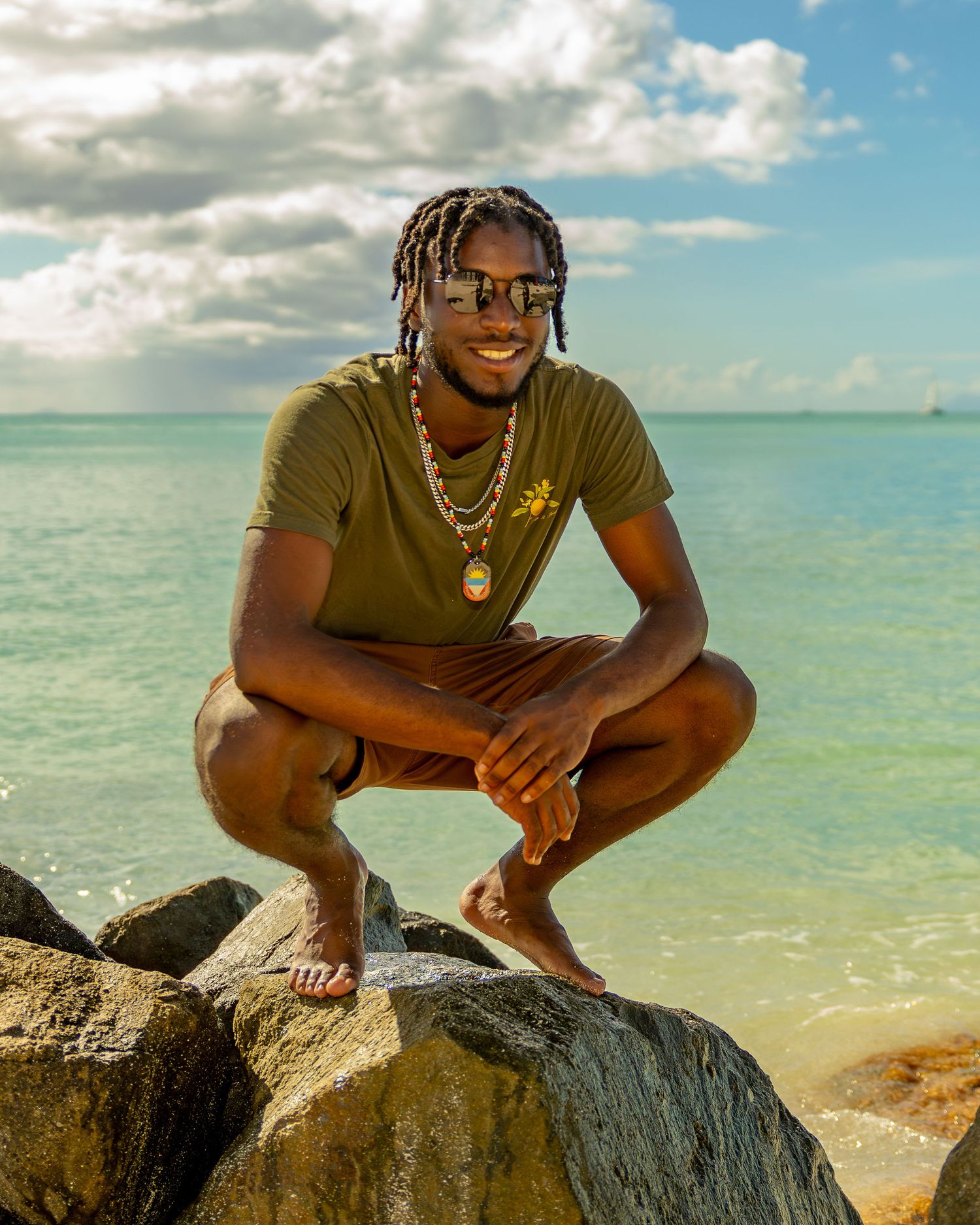 Person in olive shirt poses on coastal rocks with sparkling ocean background.