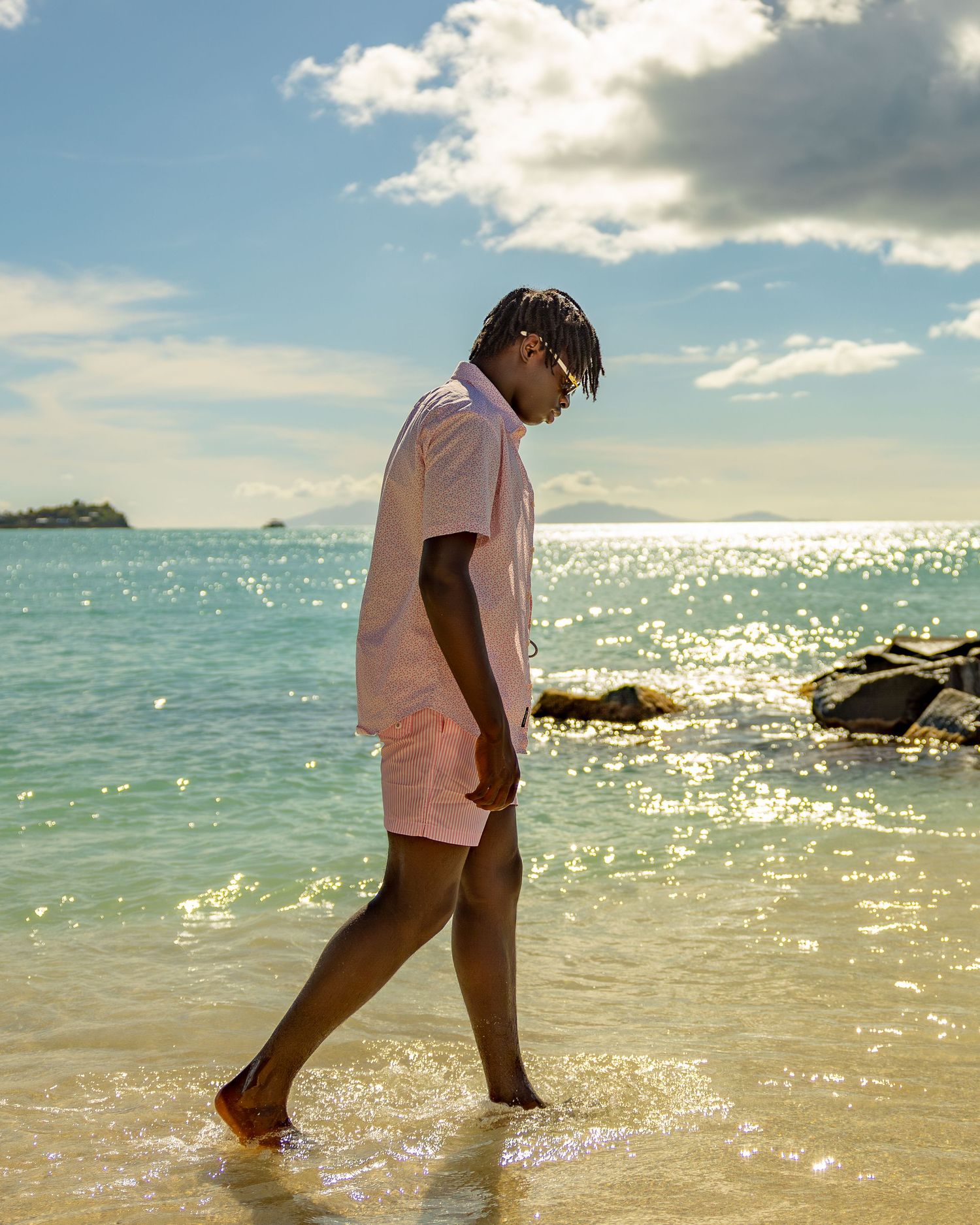 Person walking barefoot on beach wearing pink outfit with ocean waves in background.