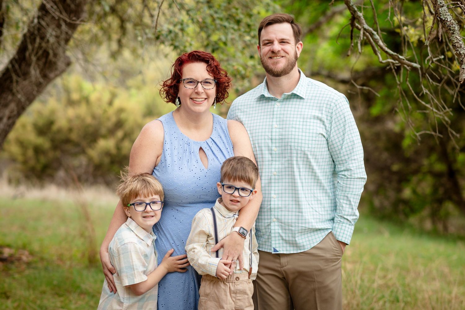 A family of four poses outdoors in coordinated casual attire against a natural backdrop with trees and foliage.