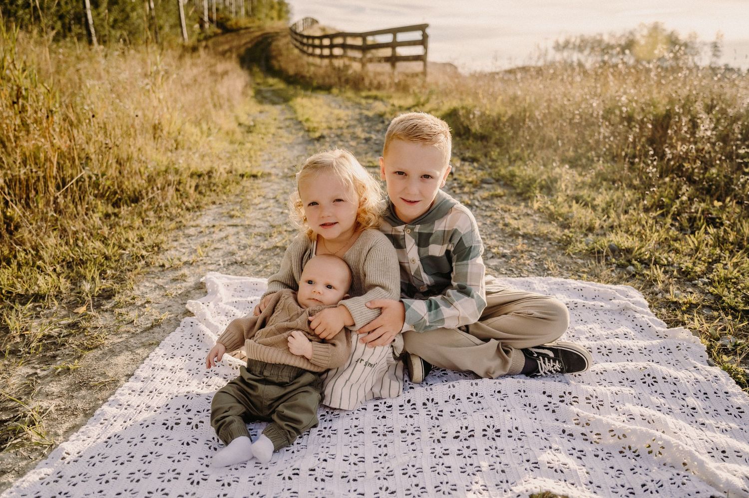 Children playing together on a patterned blanket in a sunny meadow.