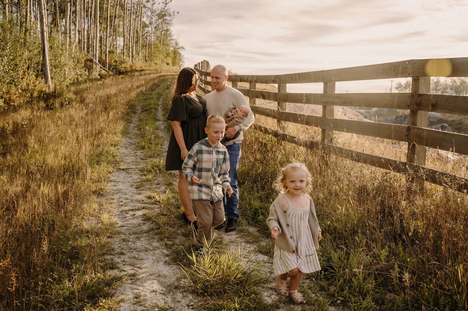 Family walking together on a dirt path beside a wooden fence.