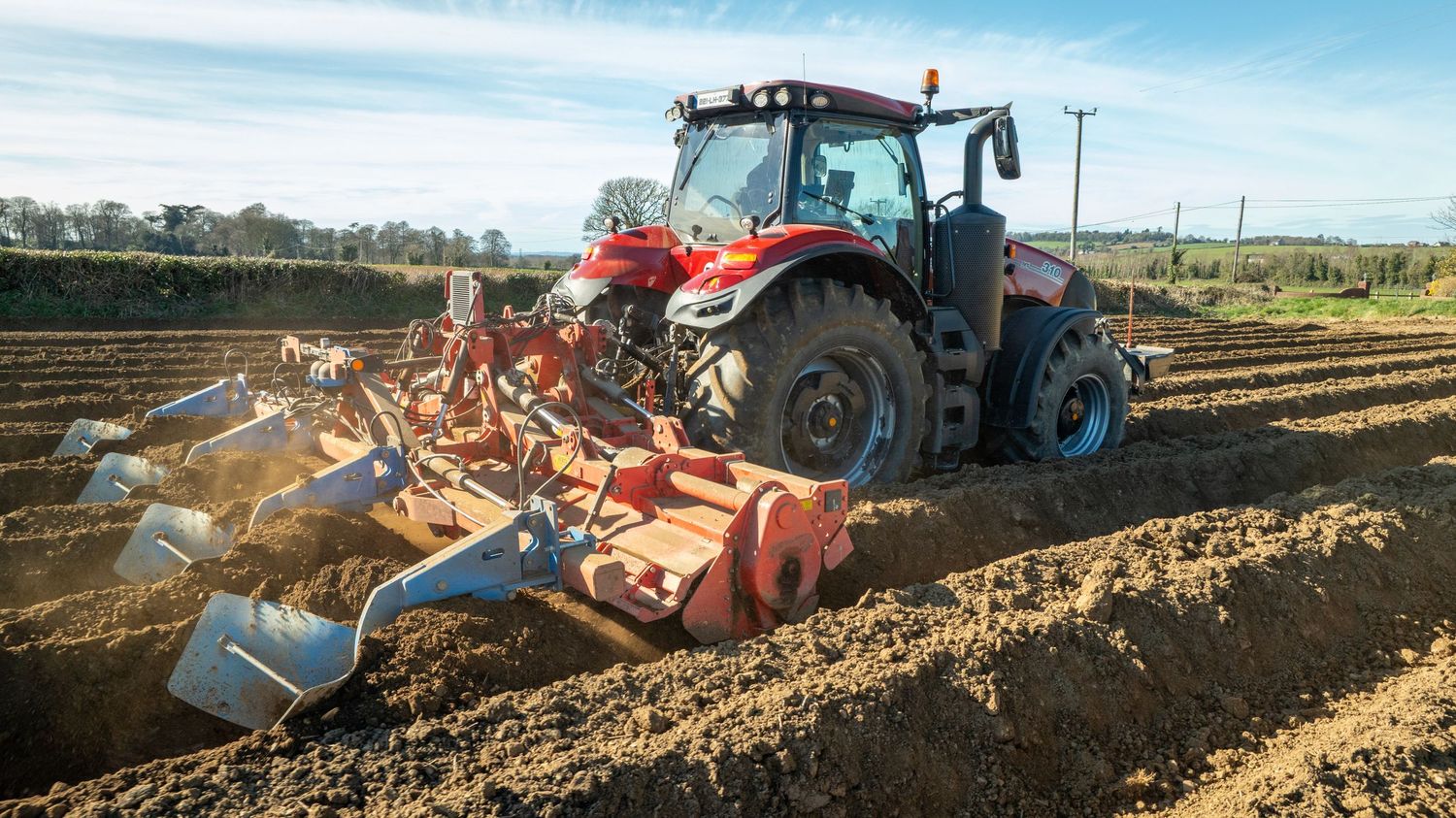 A modern blue tractor pulling agricultural equipment through freshly tilled soil in a farm field.