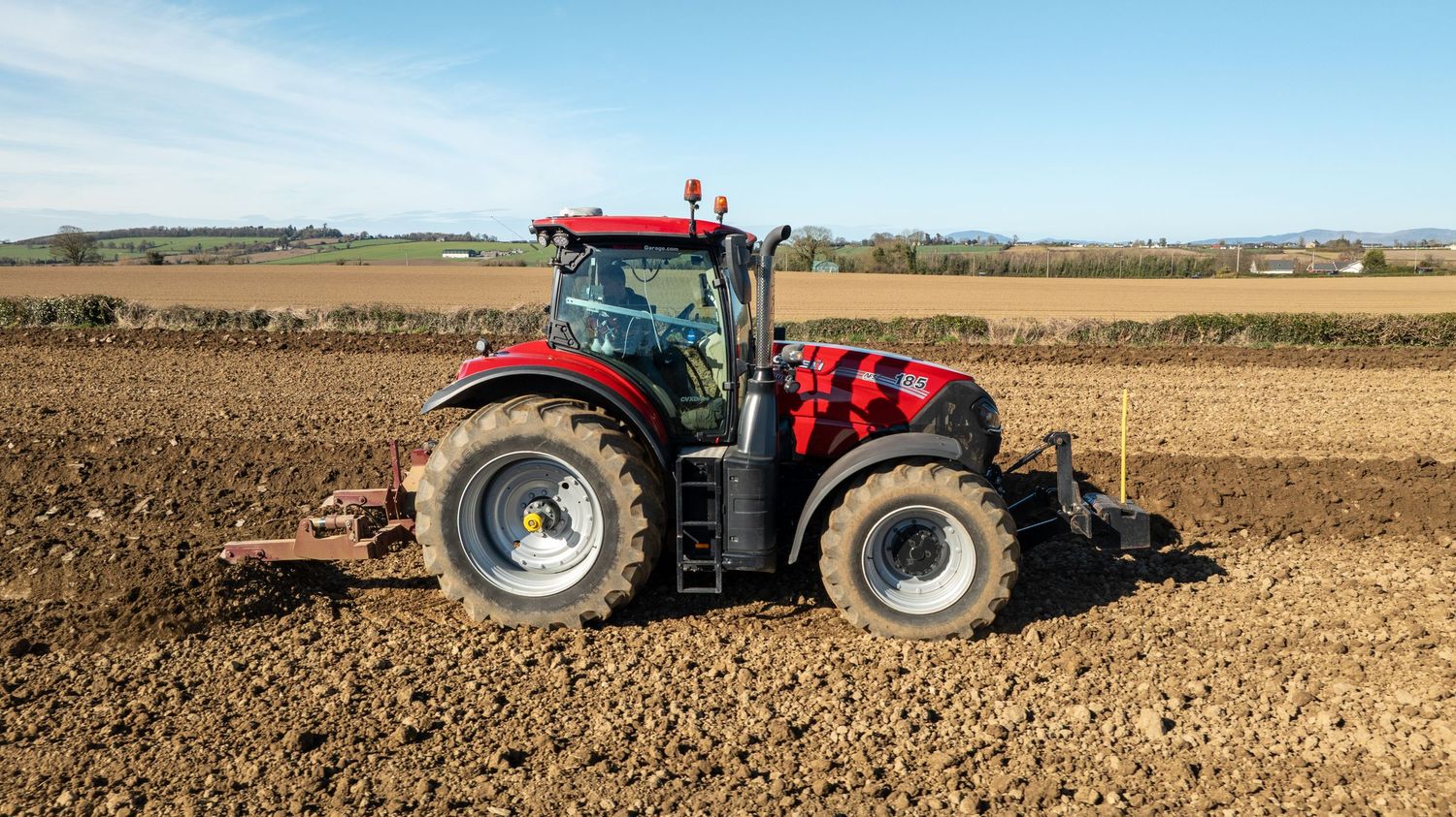 A red tractor plowing and tilling brown soil in an agricultural field on a clear sunny day.
