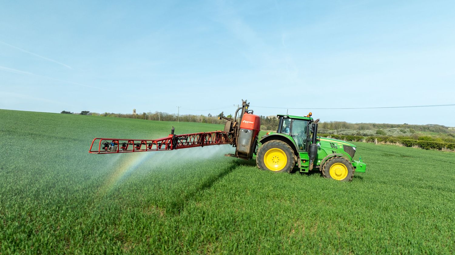 John Deere tractor spraying pesticides on a lush green agricultural field.