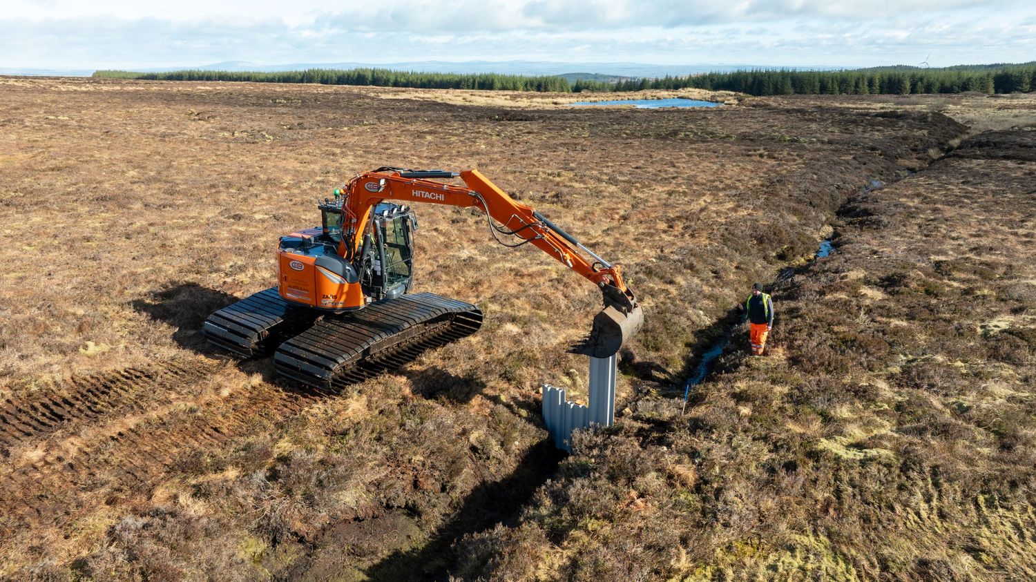 Orange excavator digging trenches in dry brown field with pipeline installation work underway.