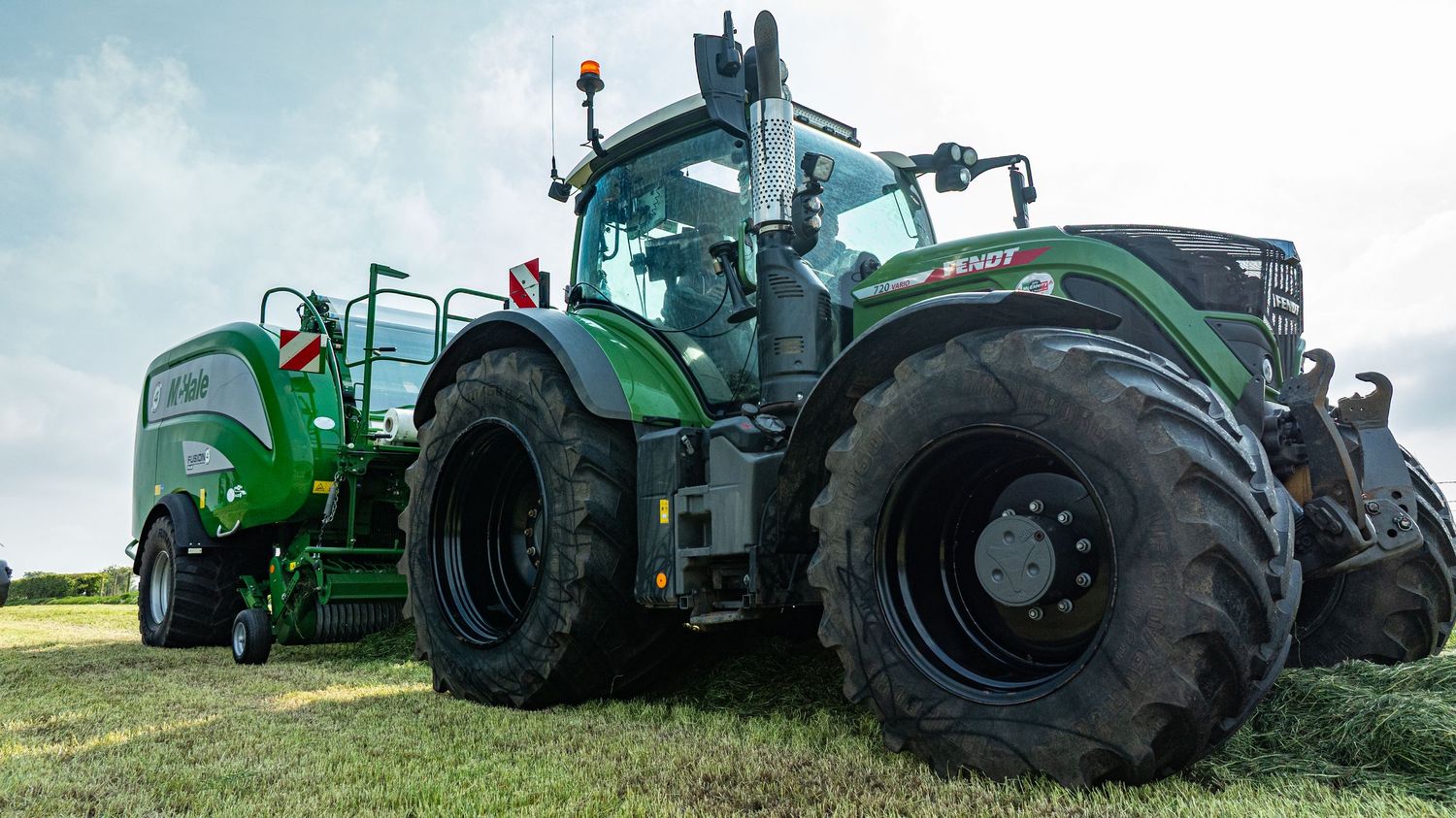 A large green Fendt tractor with massive wheels parked on grassy terrain beside a smaller agricultural vehicle.