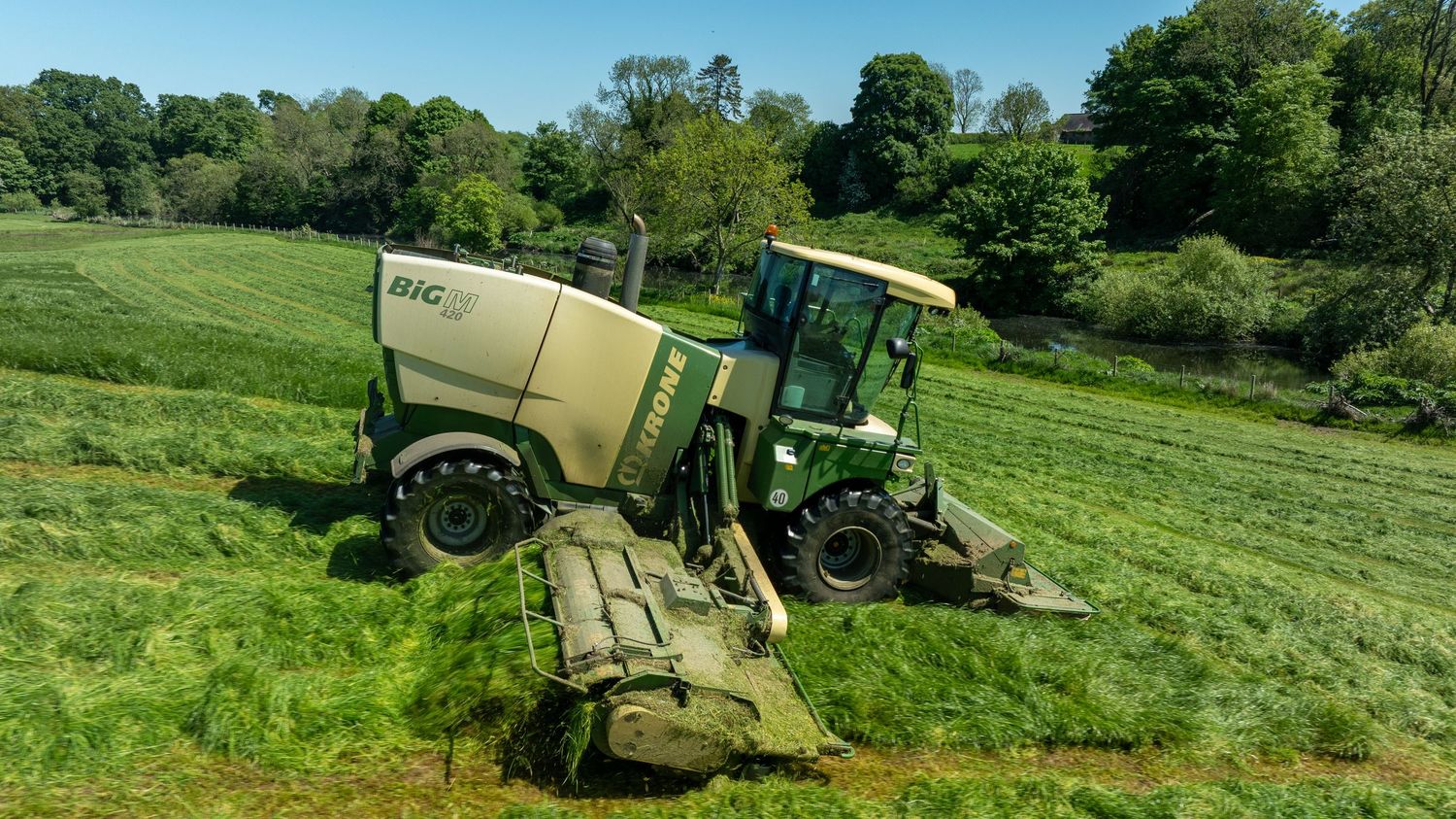 A green John Deere tractor with sprayer equipment traverses a sloping hillside field in bright sunlight.