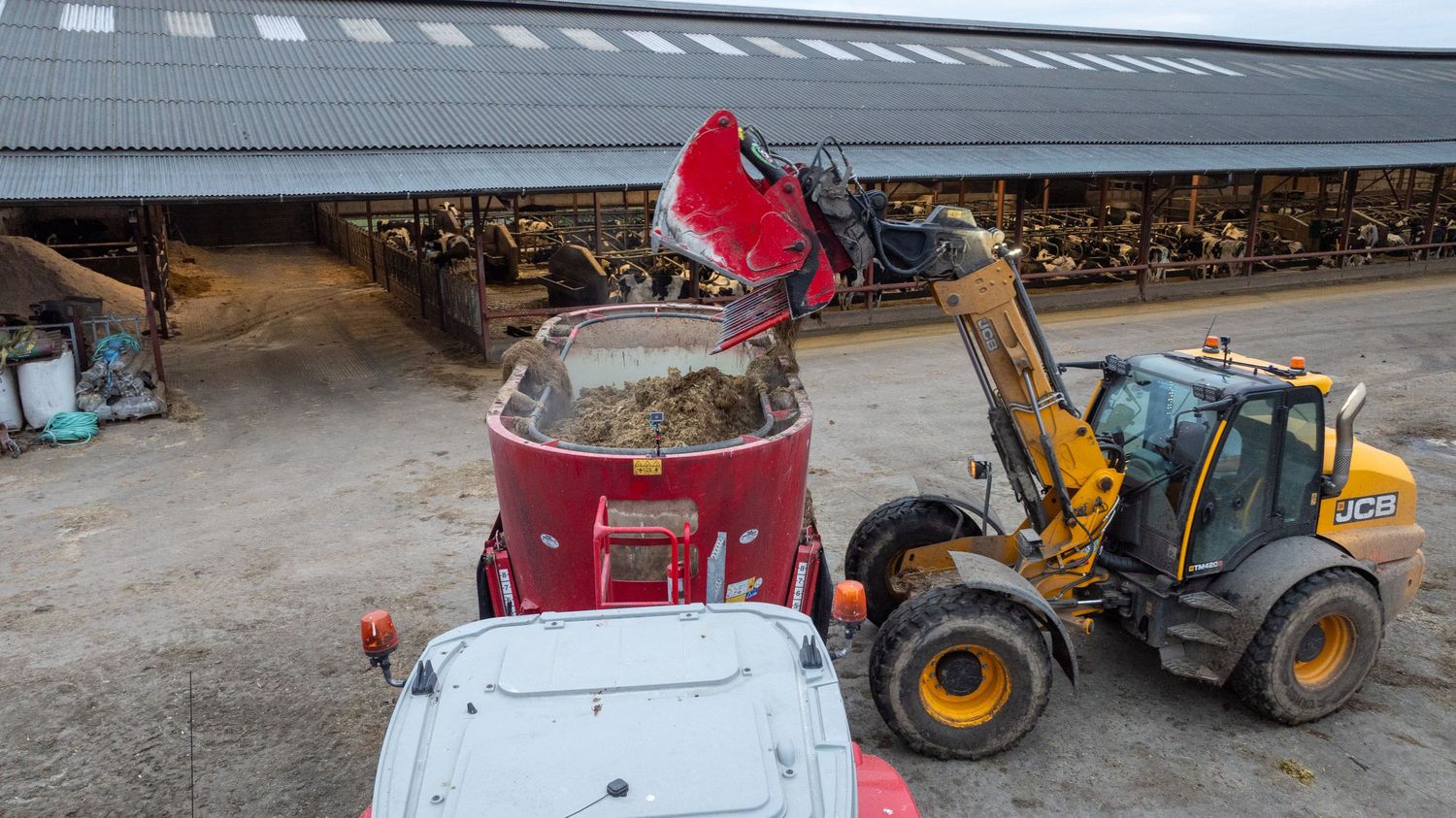 Yellow loader dumping material into a large red container at an agricultural storage facility.