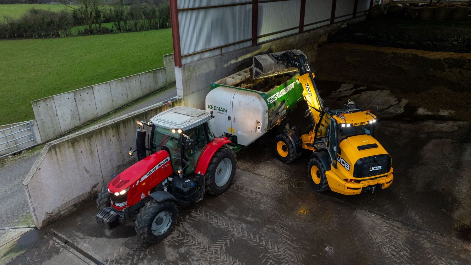 Red tractor and yellow construction vehicle working together near storage building in rural setting.