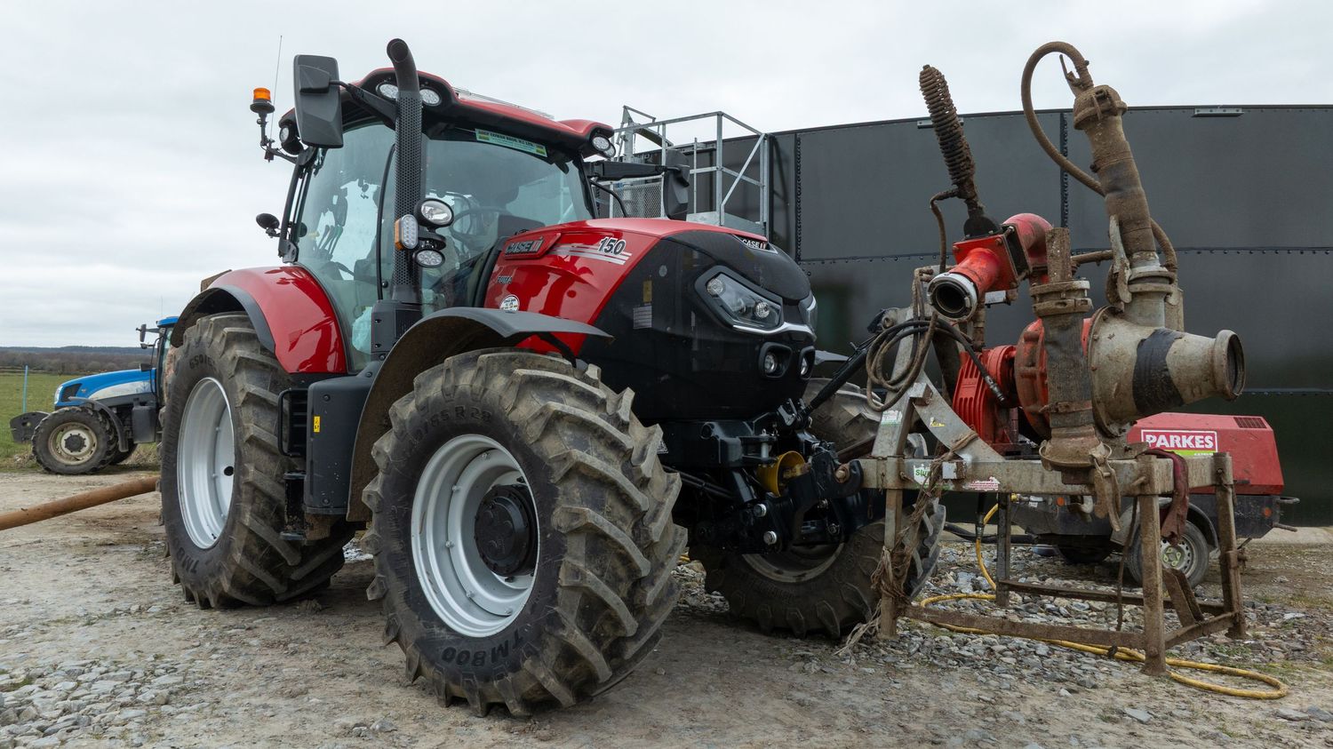 Large red Case IH tractor with forestry attachment parked on gravel surface next to dark industrial building.