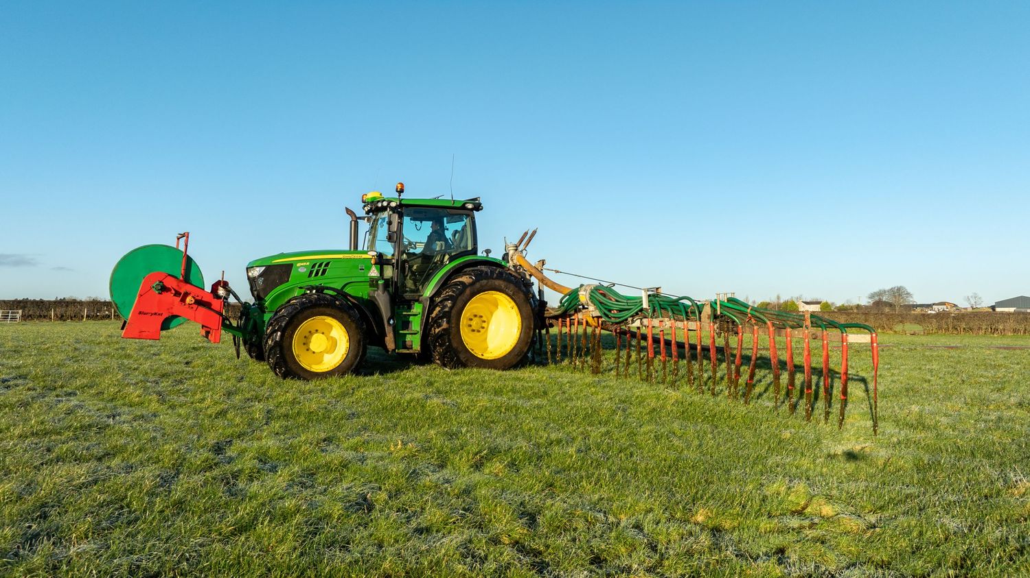 A green John Deere tractor with farming equipment sits in a lush grassy field during daylight hours.
