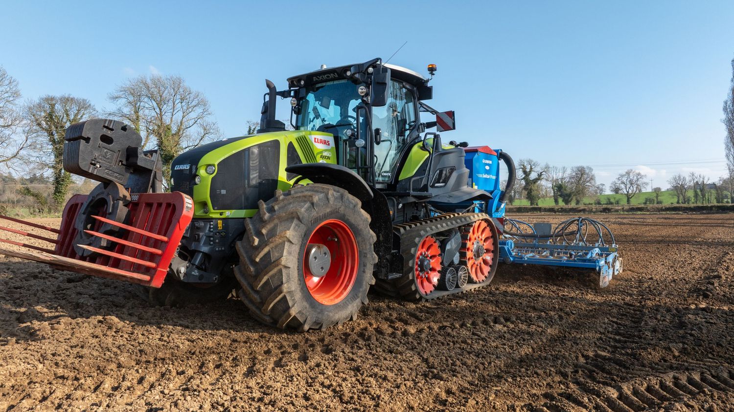 Modern CLAAS tractor with dual wheels and soil cultivation attachment working in a freshly plowed agricultural field.
