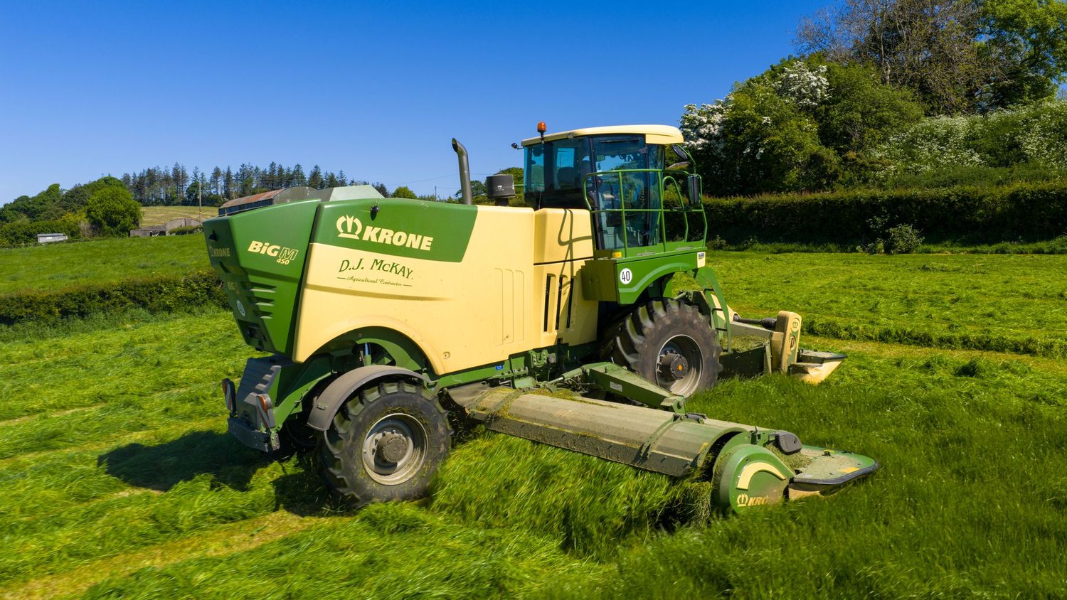 Yellow Krone forage harvester equipment parked in a lush green hillside field during agricultural operations.