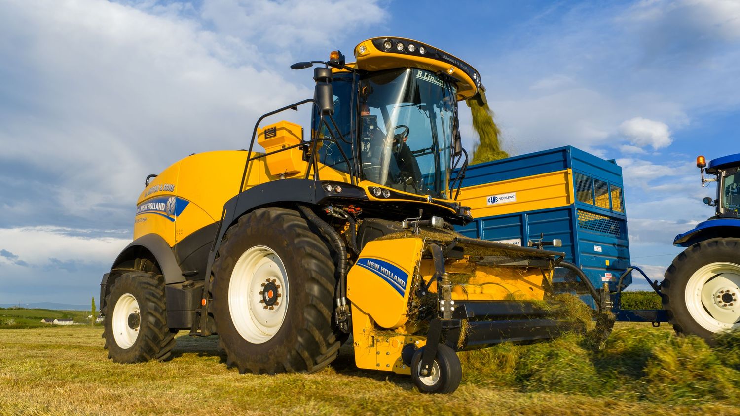 Yellow and blue New Holland CR combine harvester on a field under blue sky with white clouds.