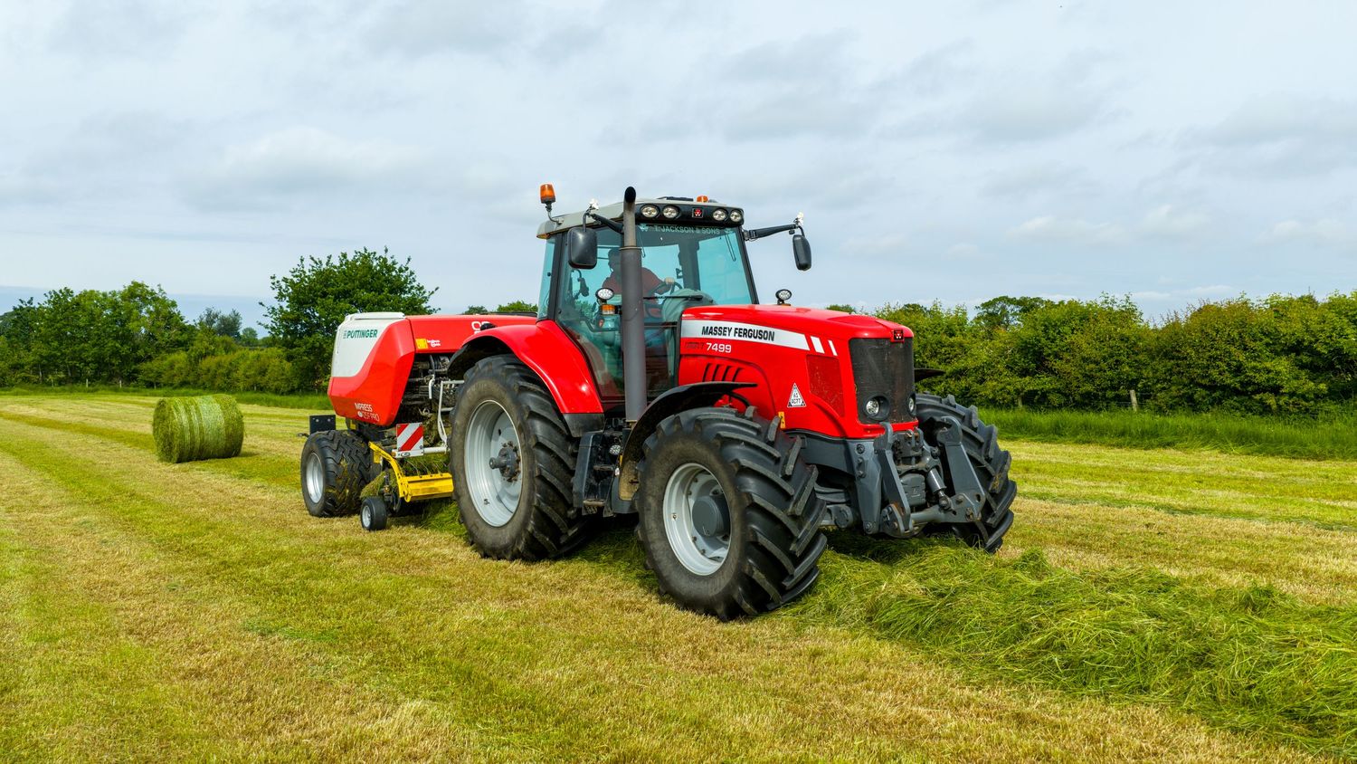 Red Massey Ferguson tractor pulling baler equipment across green farm field under cloudy sky.