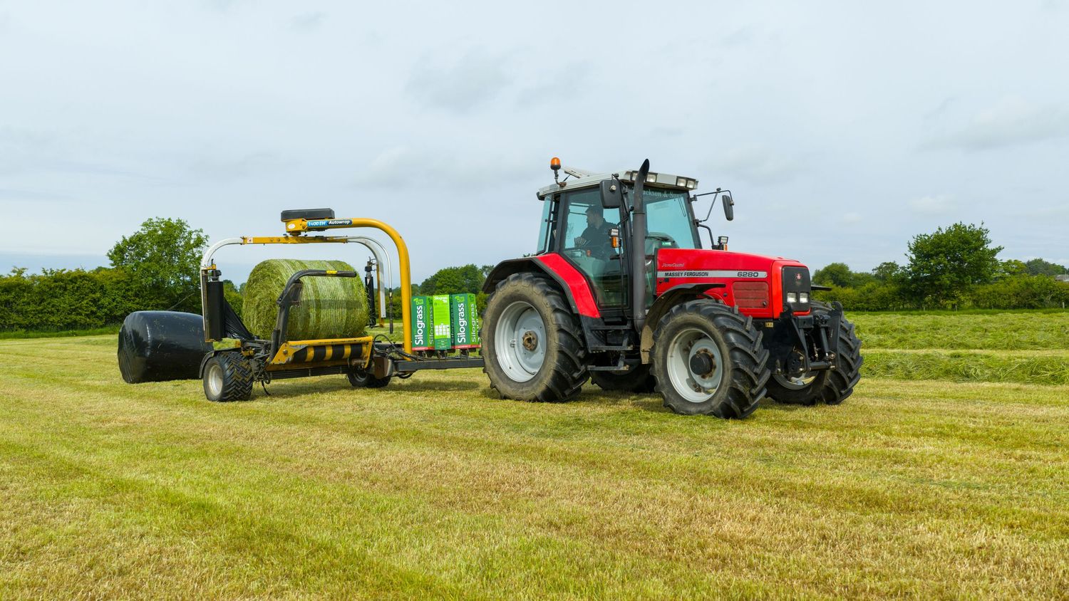 Red Massey Ferguson tractor with baler equipment working in green agricultural field during hay baling operation.