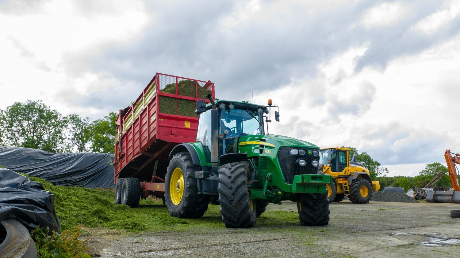 A panoramic view of farm tractors and equipment lined up on a rural property against a cloudy sky.