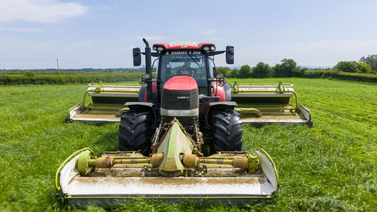 Agricultural machinery performs mowing operations on lush green farmland across multiple stages of field work.
