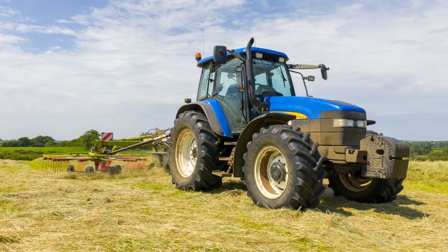 A series of agricultural tractors working in farm fields under blue skies with farmland and rolling hills in the background.