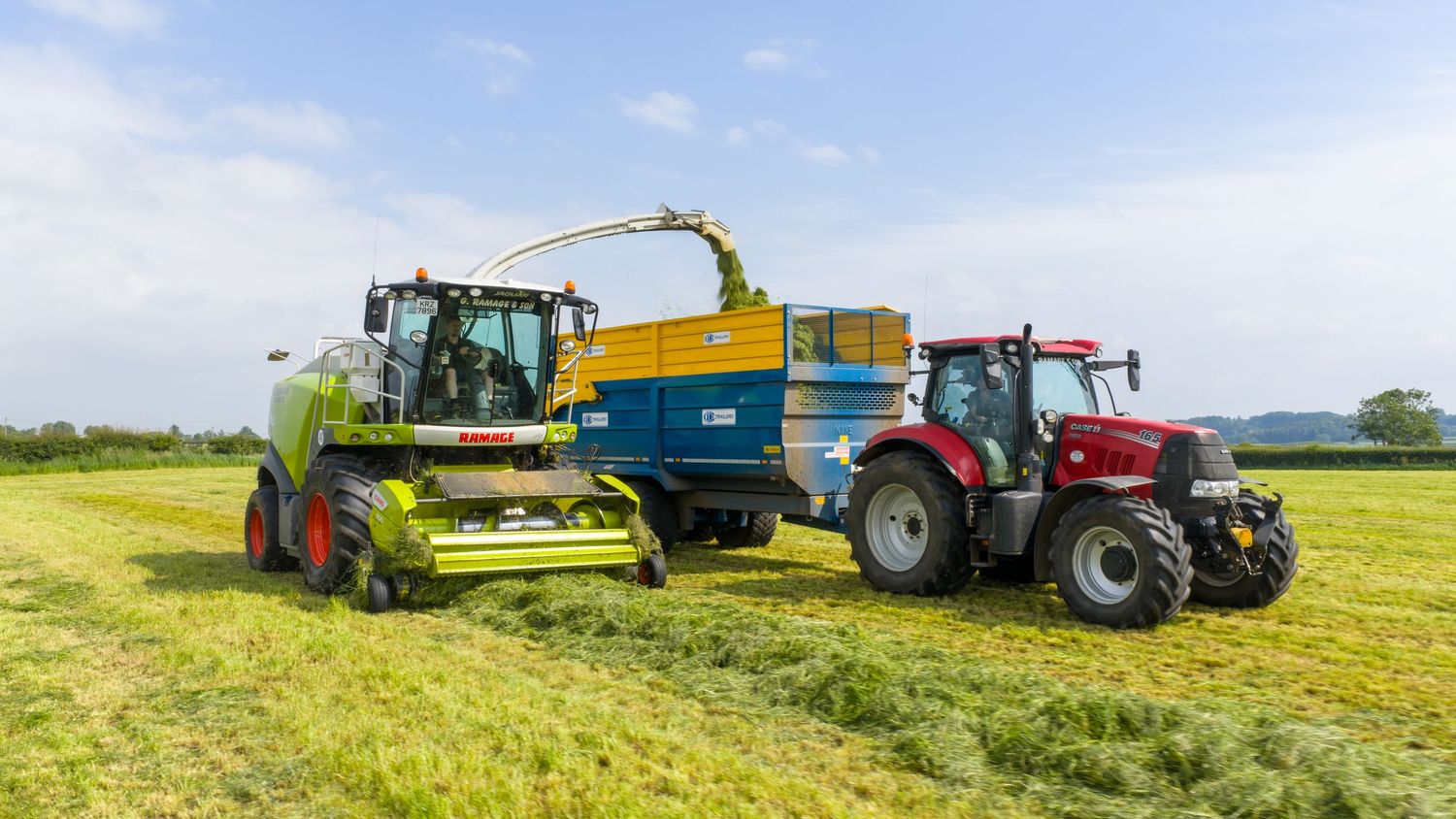 Modern combine harvesters and tractors working together to harvest crops in a golden agricultural field under blue sky.