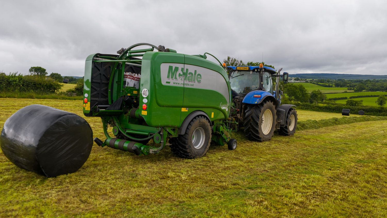Large agricultural machinery equipment working in green farm fields during harvest season under cloudy skies.