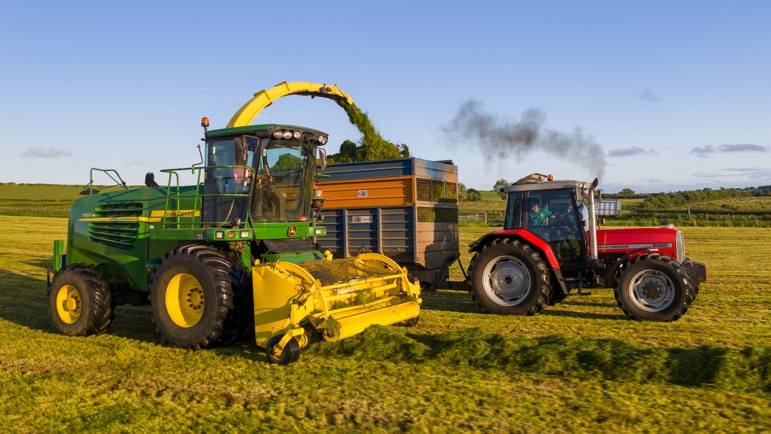 Variety of agricultural tractors and machinery working in golden harvested fields under blue sky.