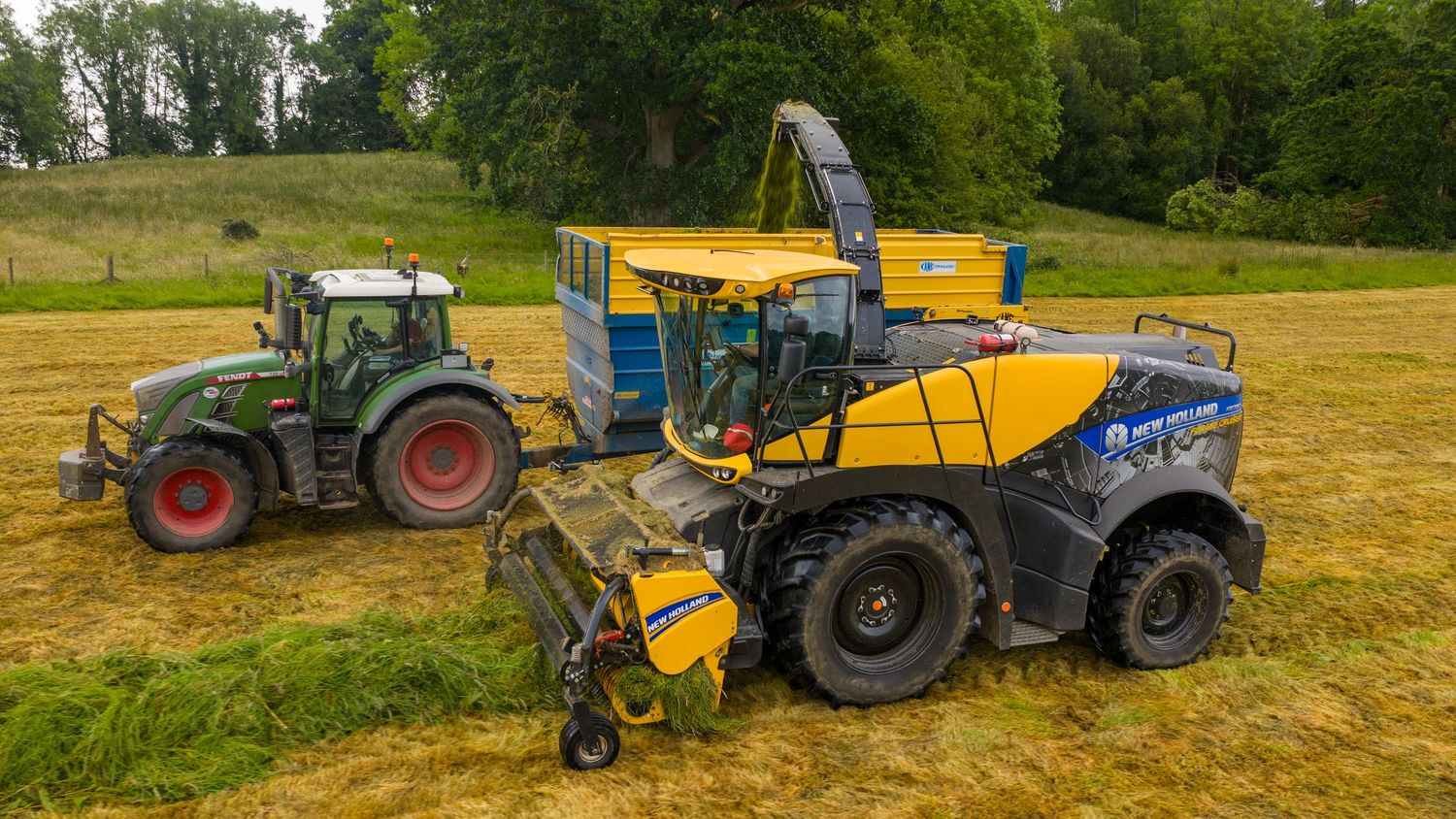 Agricultural machinery including a green tractor and yellow harvester working together in a grassy field.