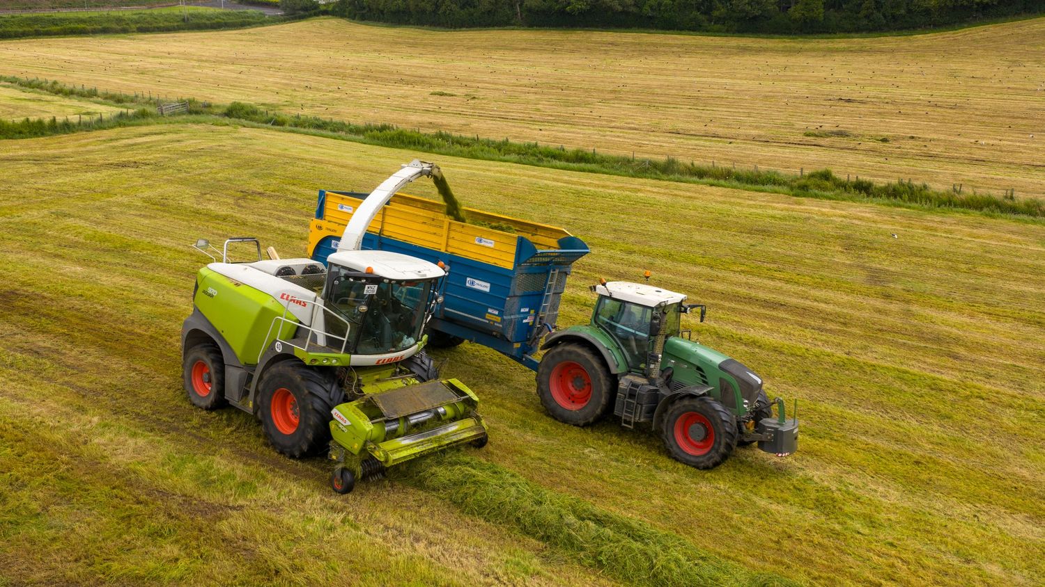 Aerial view of a combine harvester transferring grain to a tractor with trailer in golden wheat field.