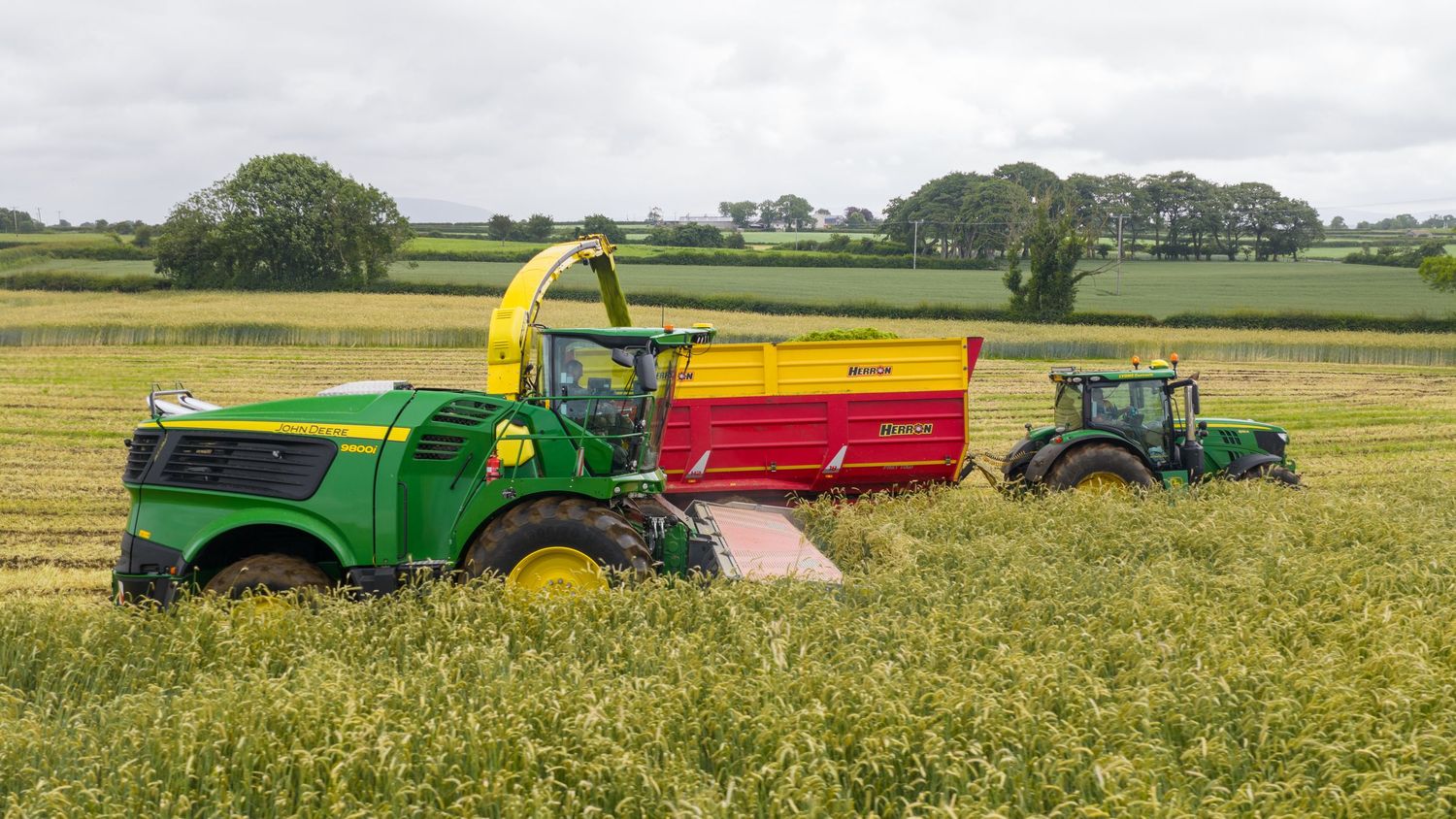 A series of tractors and farm equipment work across golden wheat fields during harvest season.