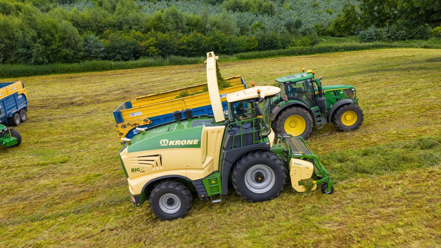 Aerial view of green and yellow farming equipment working in a grassy agricultural field.