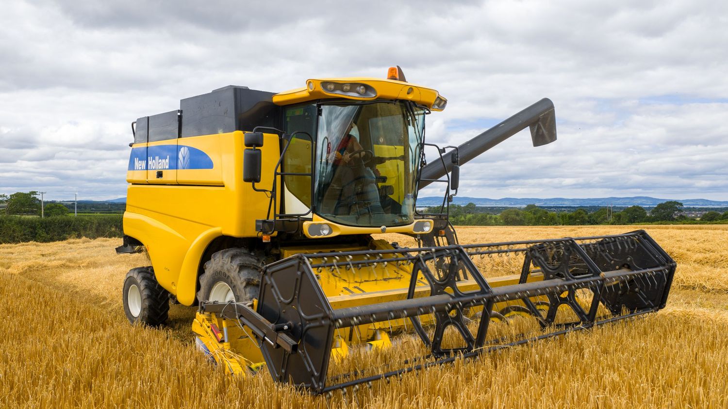 Yellow combine harvester working in golden wheat field under cloudy sky during harvest season.