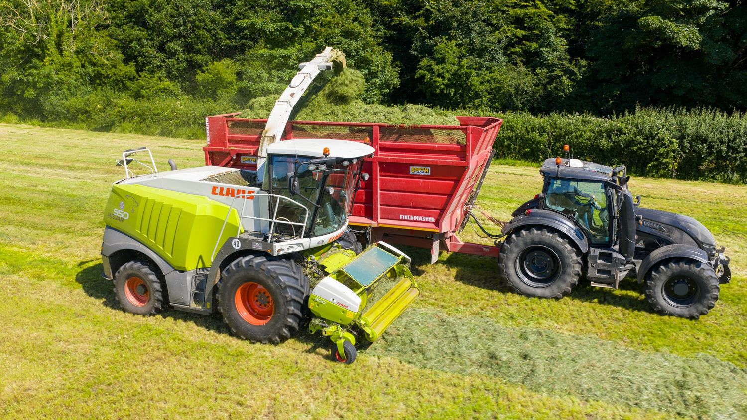 Tractors and farming equipment working together in a lush green agricultural field during harvest season.