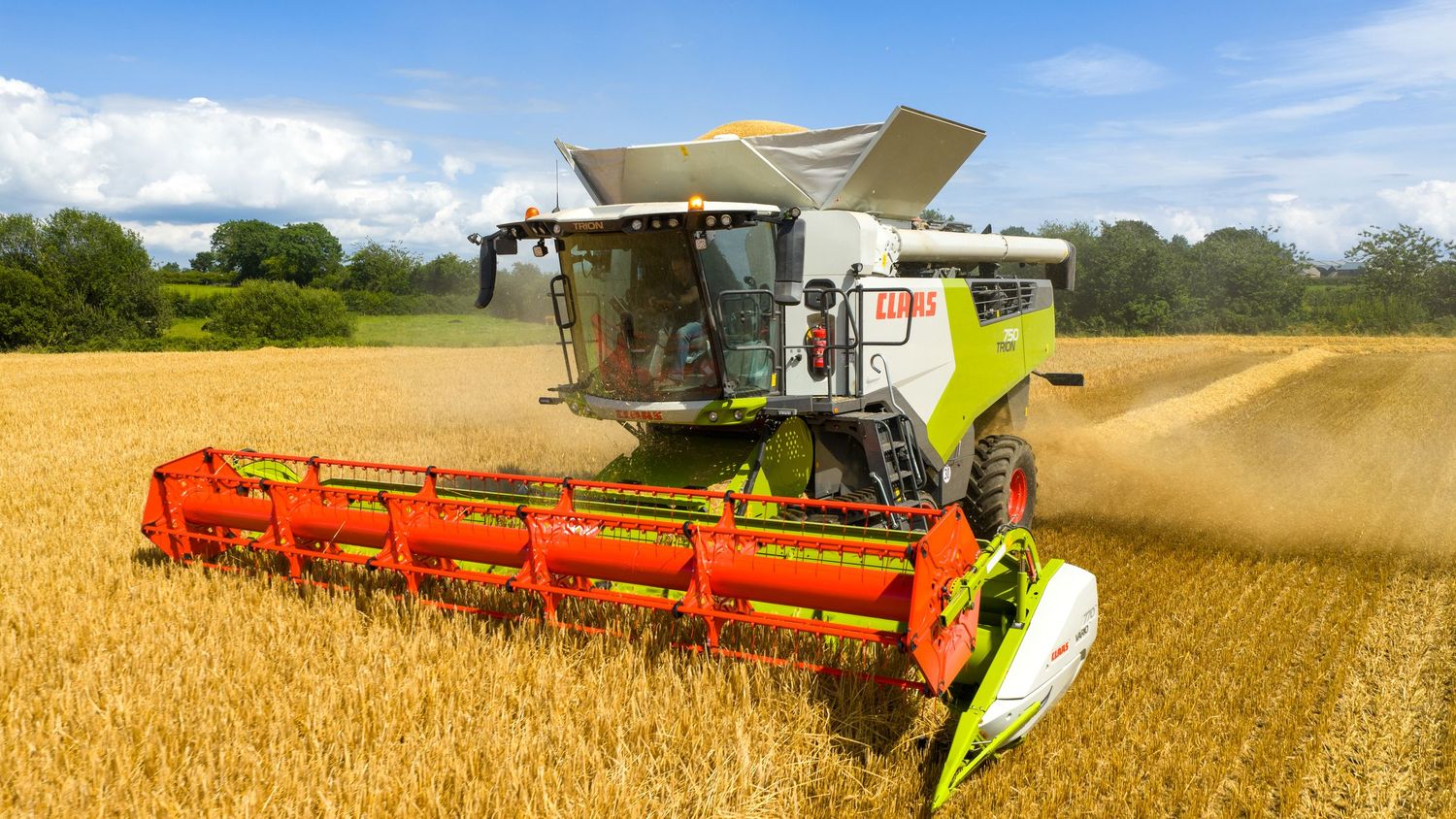 Modern combine harvester with bright orange header attachment working in golden wheat field under blue summer sky.