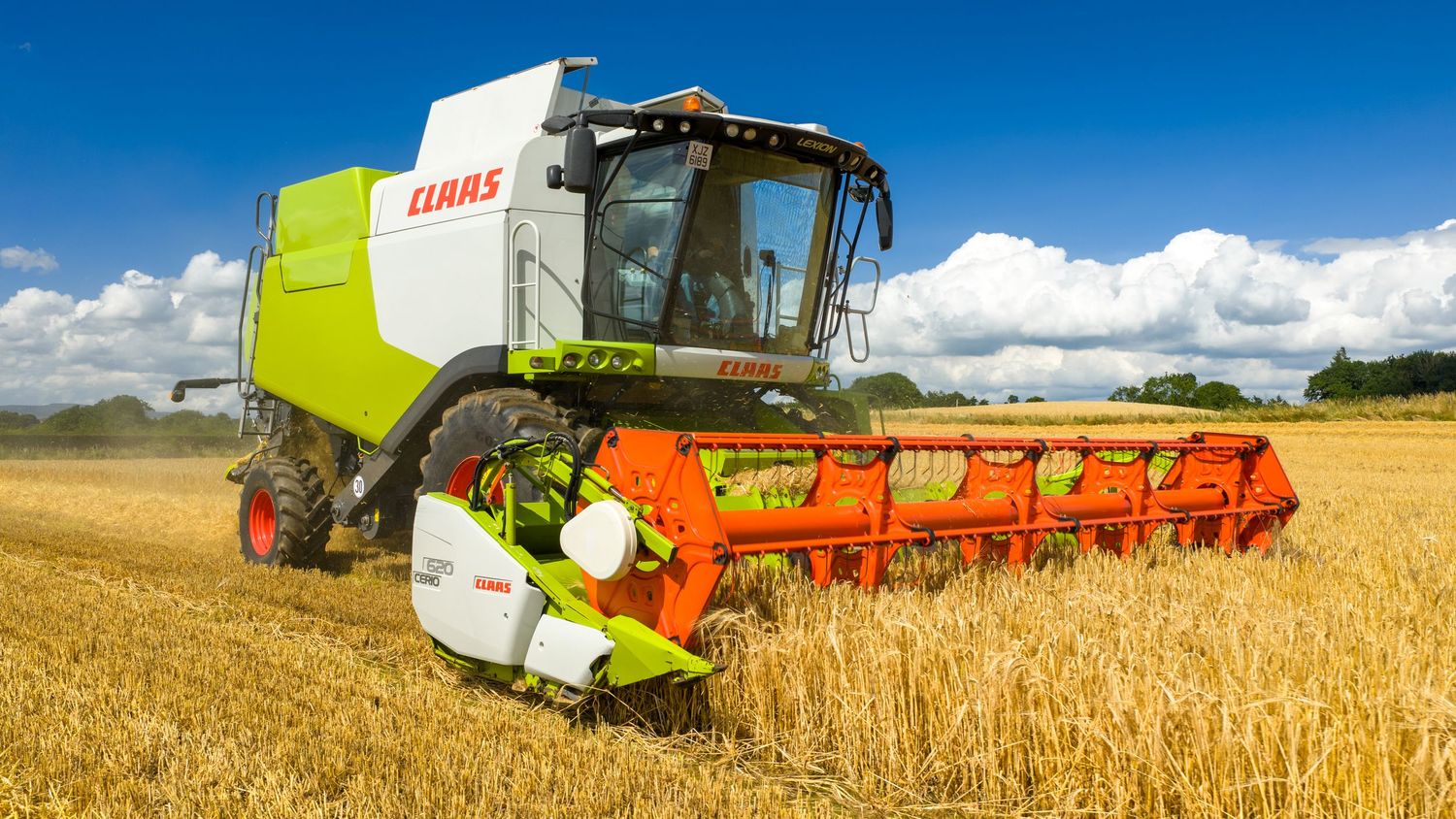 A panoramic view of combine harvesters working in golden wheat fields under a bright blue summer sky.