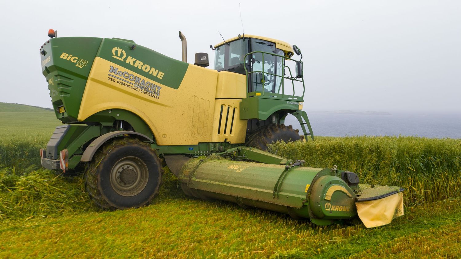 Large yellow Krone combine harvester parked on a grassy hillside with attached header during harvest time.