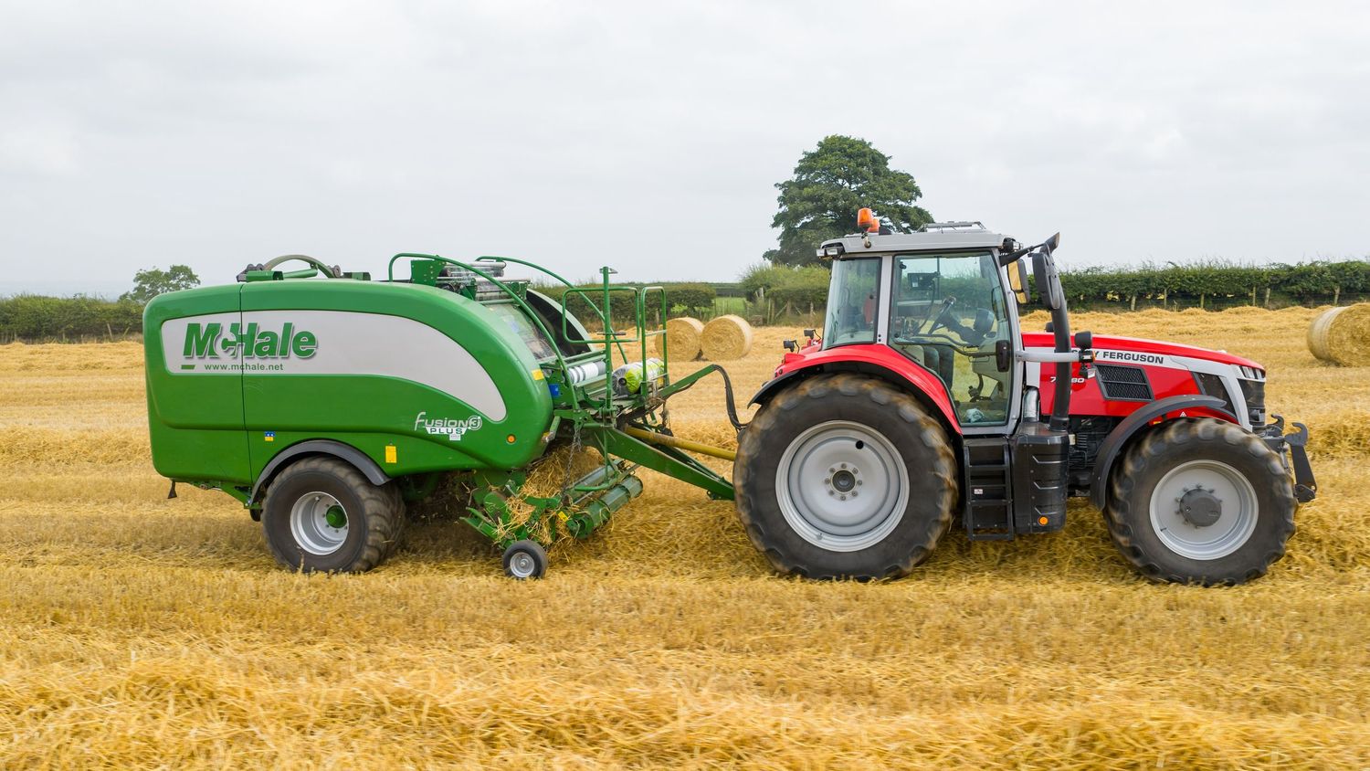 Red Massey Ferguson tractor operating a McHale baler in harvested wheat field during agricultural operations.