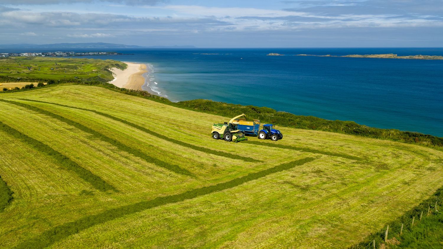 Scenic panoramic view of a green coastal landscape with grassy fields stretching along the bright blue ocean shoreline.