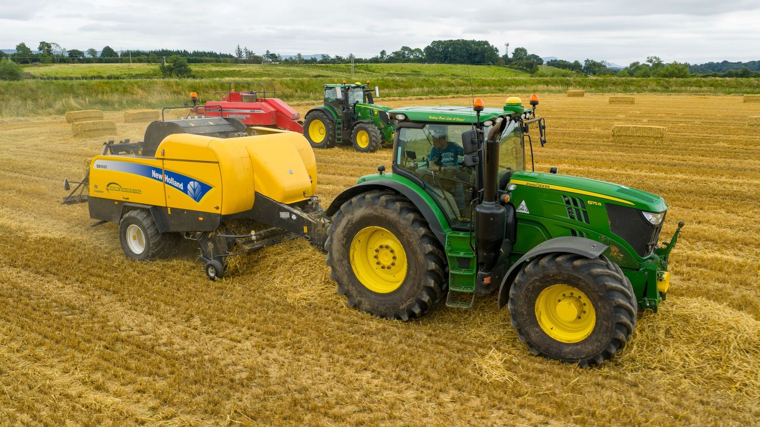 John Deere tractor pulling hay baler machinery across golden wheat field during harvest season.