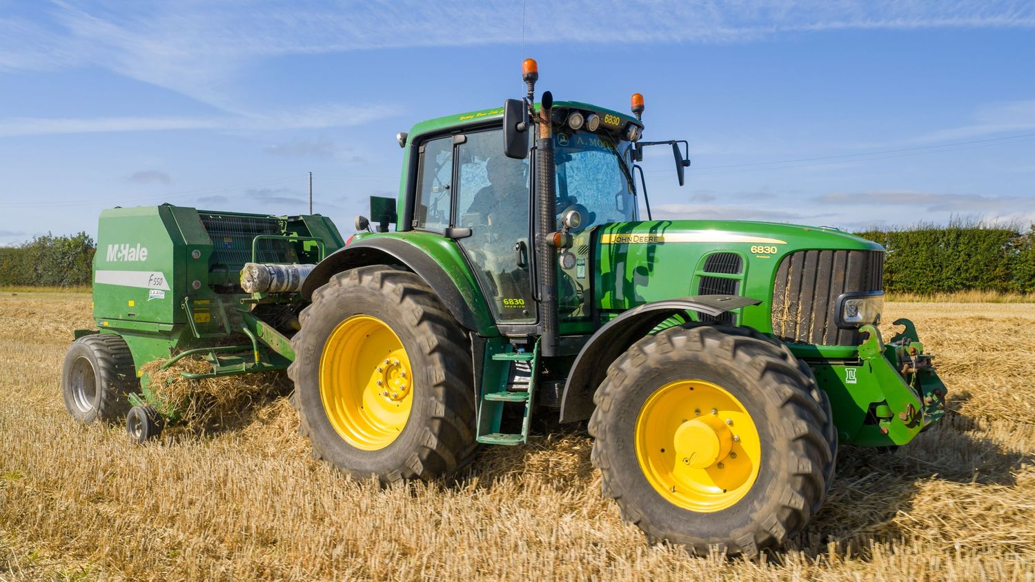 Green John Deere tractors line up along a golden wheat field during harvest time.