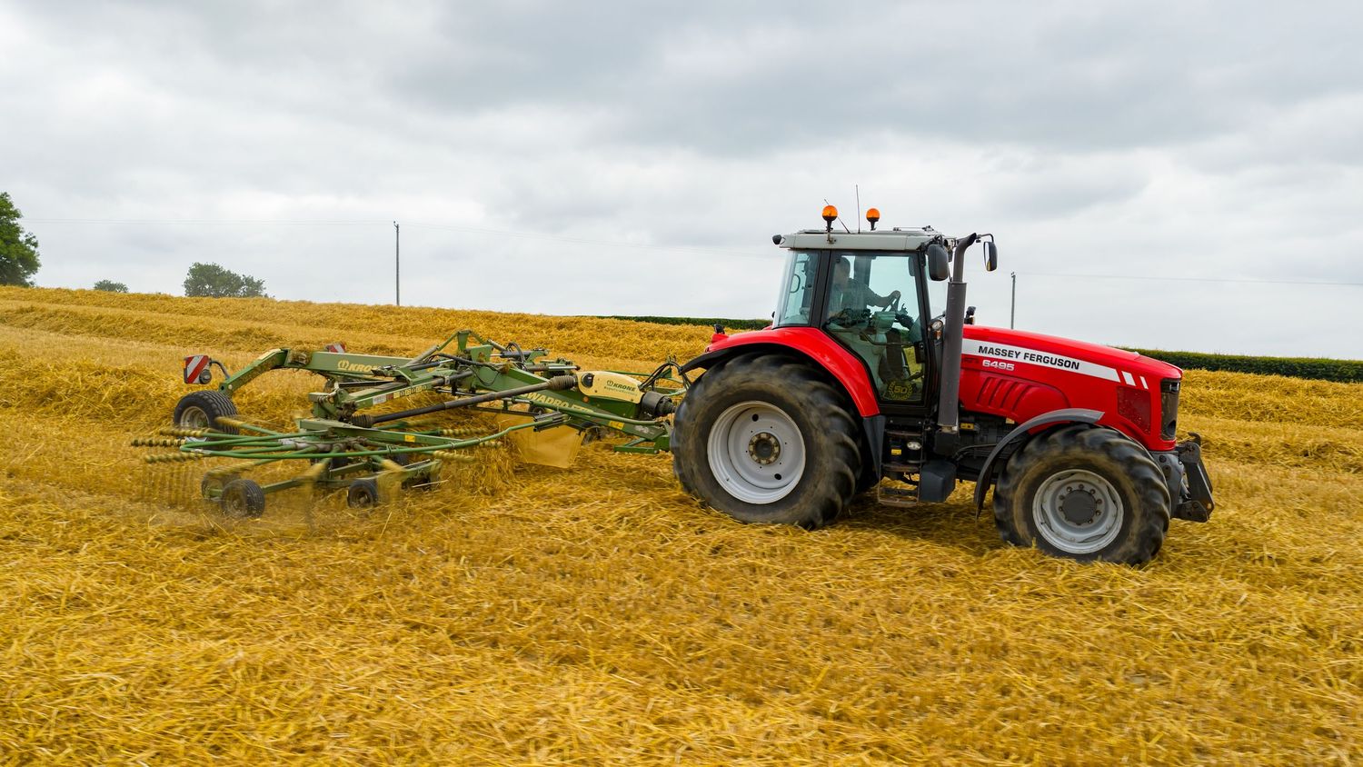Red Massey Ferguson tractor pulling tillage equipment across a golden harvested field under cloudy skies.