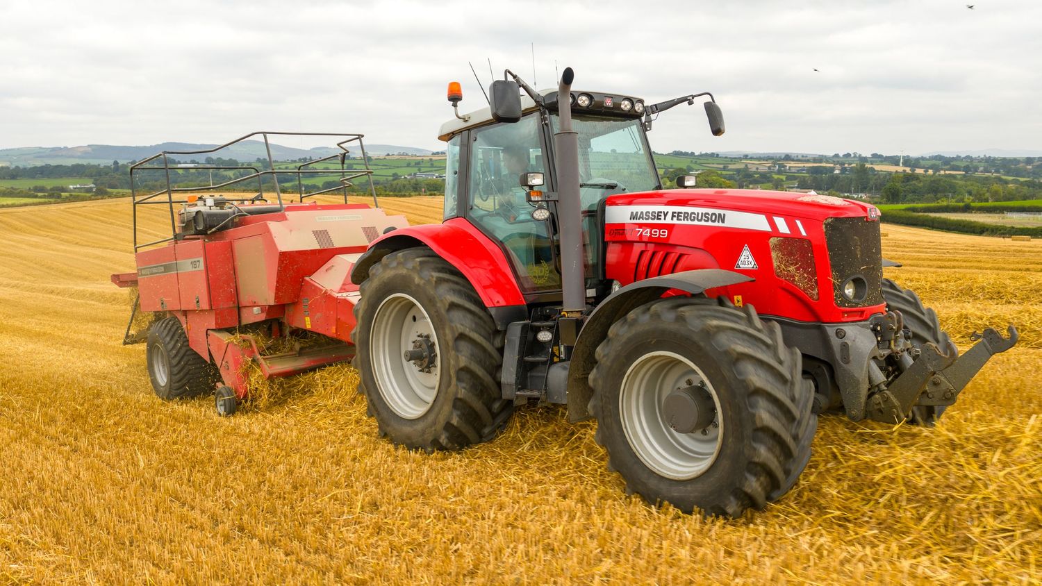 Panoramic view of modern agricultural machinery harvesting golden wheat fields under a cloudy sky.