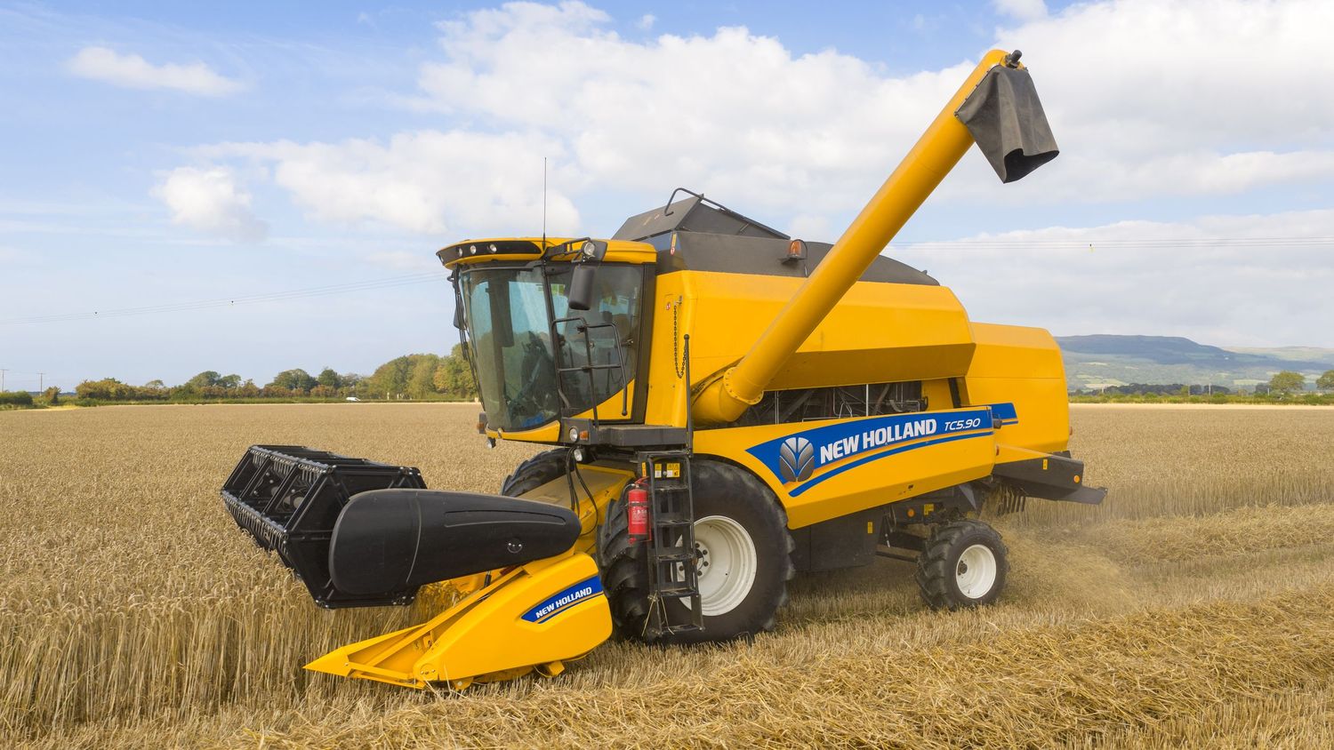 Yellow New Holland combine harvester working in wheat field with grain auger extended during harvest season.