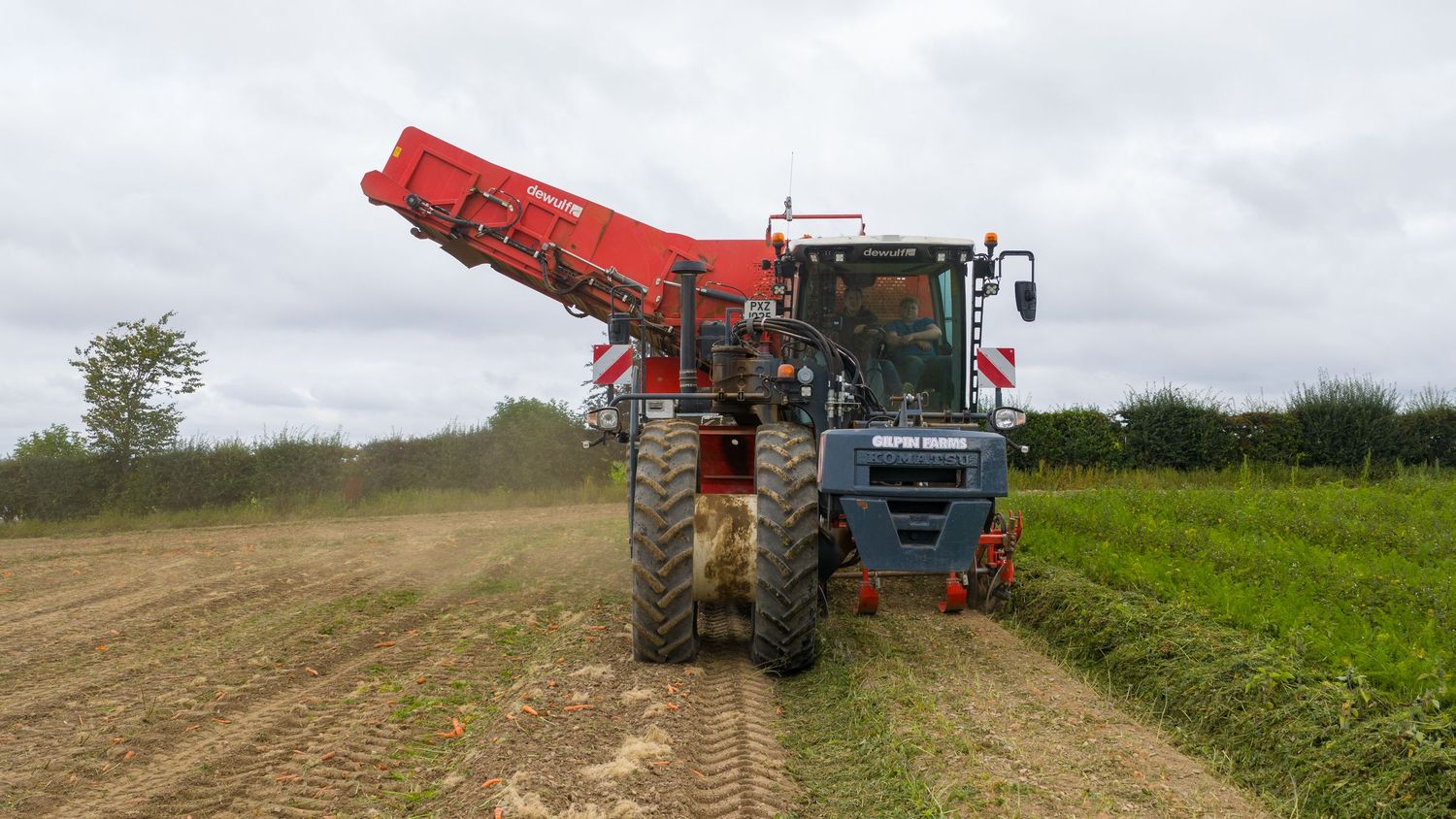 Multiple tractors and farm machinery work in sequence across a brown agricultural field during plowing operations.