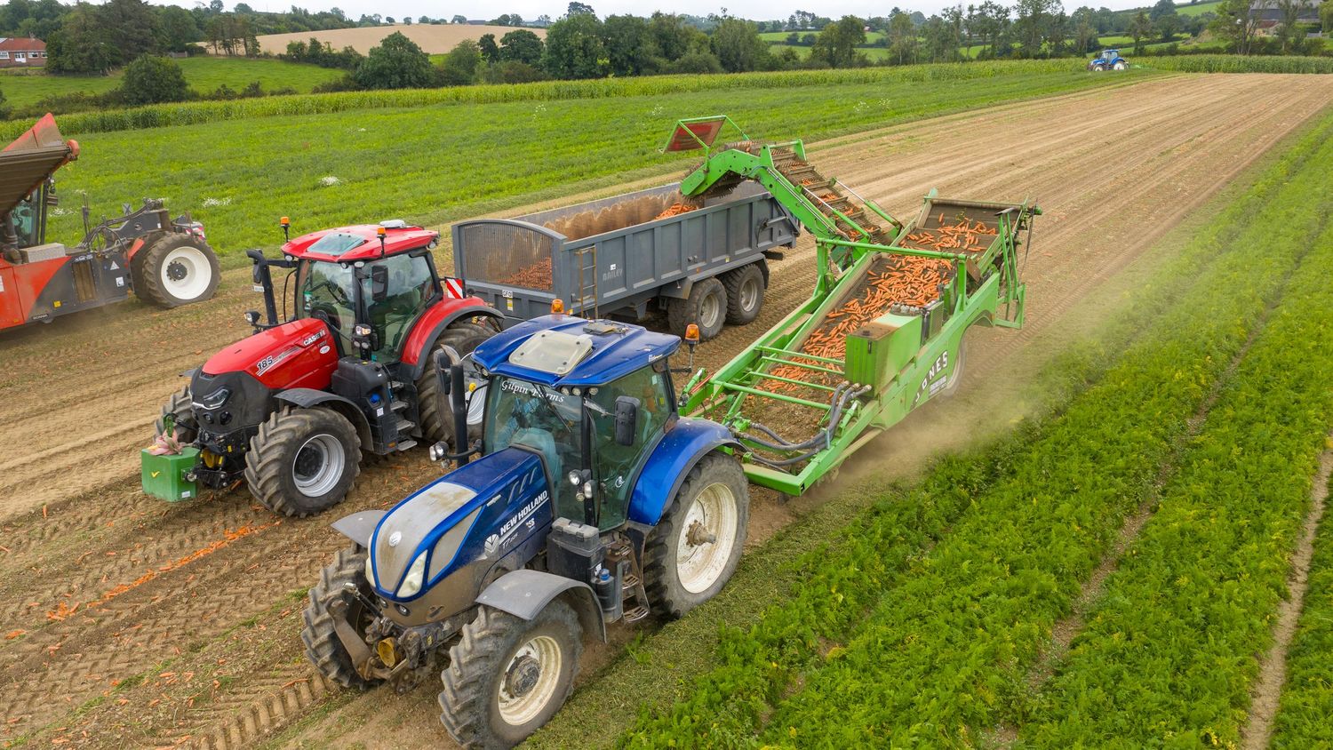 Aerial view of tractors and agricultural machinery harvesting crops in a green field during farming operations.