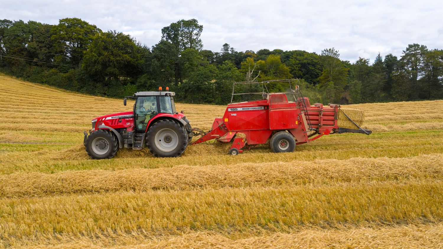 Red tractor pulling baler equipment across golden harvested wheat field on sunny summer day.