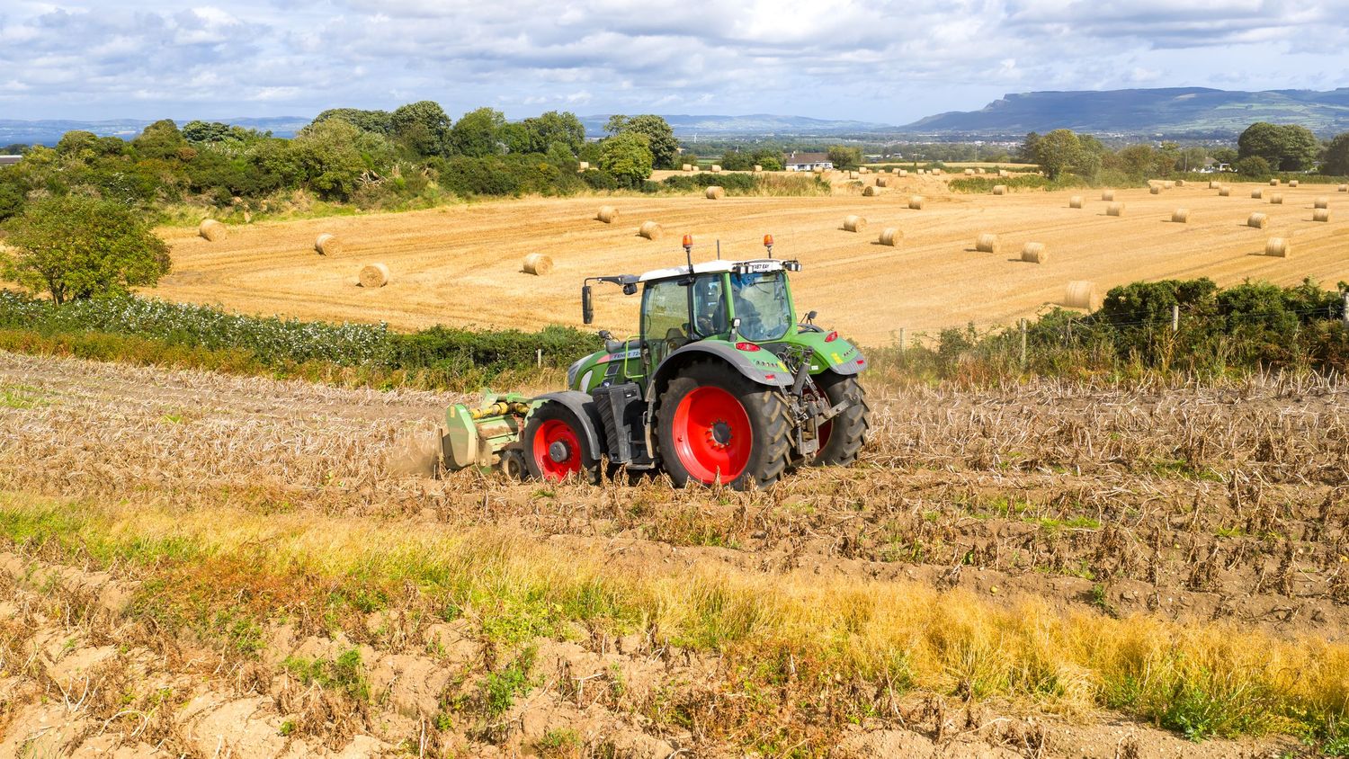 Aerial panoramic view of agricultural landscape showing harvest fields, farm machinery and rolling countryside.