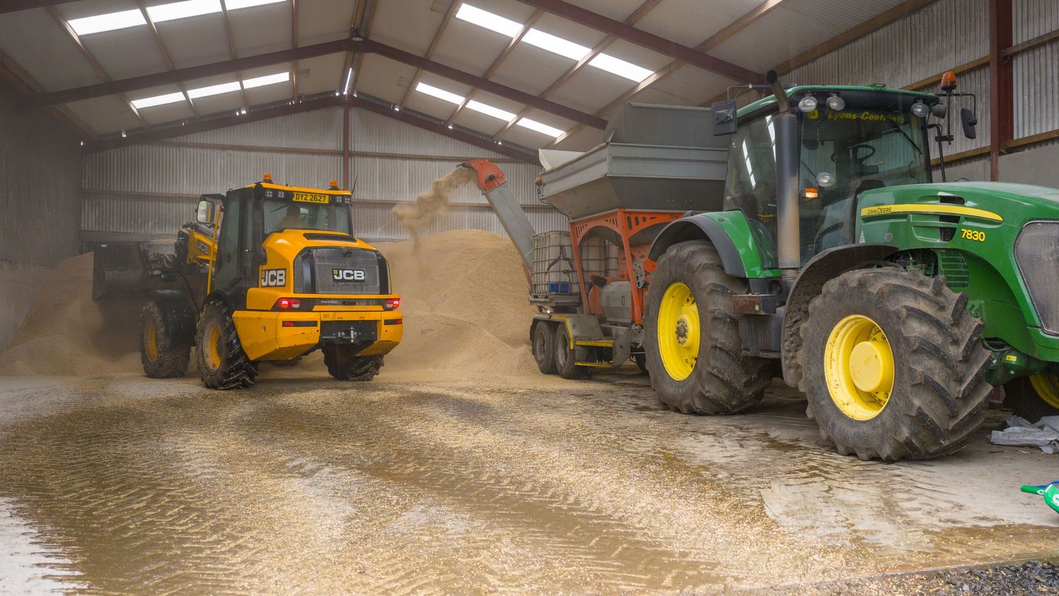 Heavy farm equipment and machinery lined up inside a large agricultural storage barn with concrete floor.