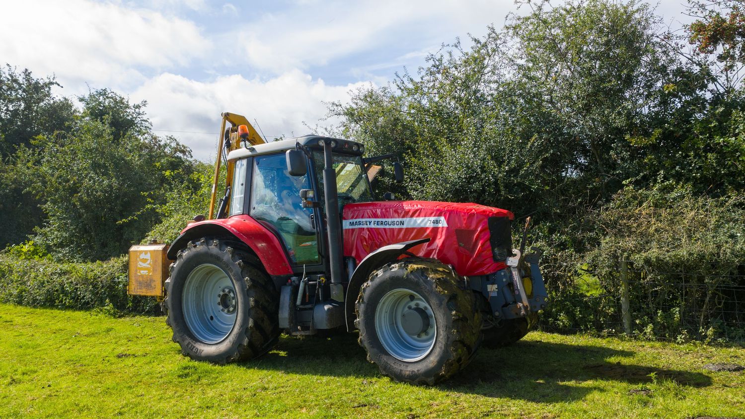 A panoramic view of red tractors and farming equipment lined up on lush green countryside pasture.